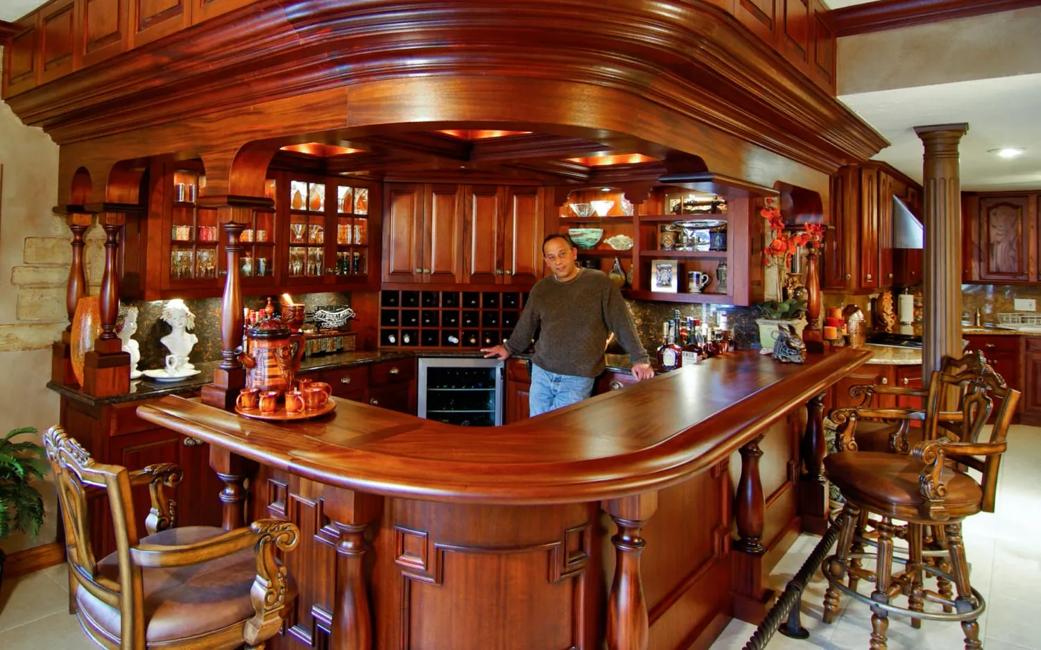 Founder Andrew Faraone behind a custom carved mahogany bar he built — turned columns, raised-panel cabinetry, and a curved bar top