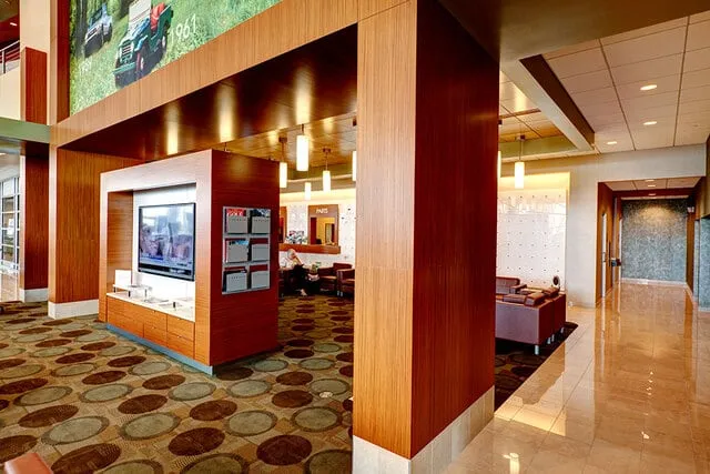 Auto dealership lounge with warm wood paneling, a media display wall, and clad columns