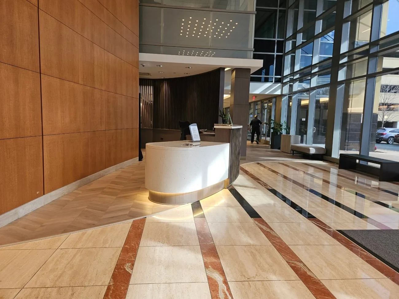 Corporate lobby with a curved custom reception desk, wood-paneled feature wall, and marble flooring