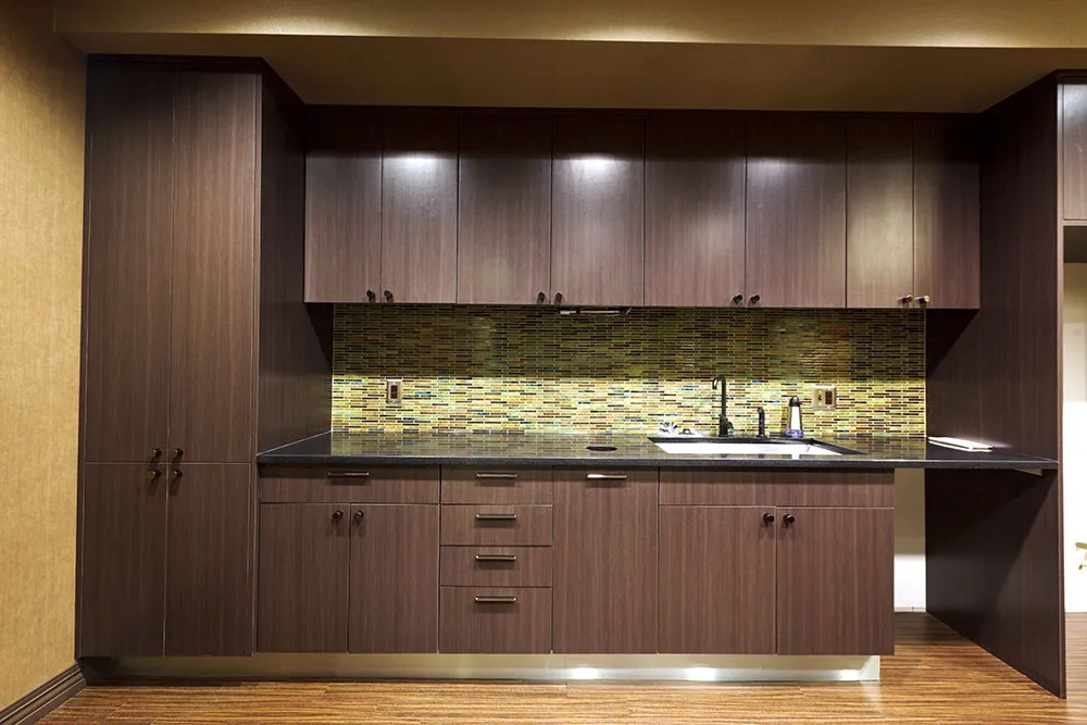 Commercial break-room casework with a black granite counter and a glass-mosaic backsplash