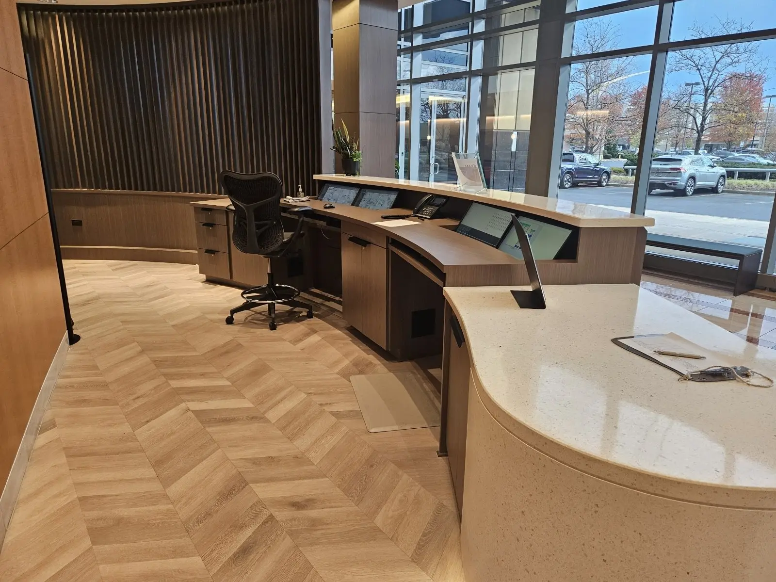 Curved custom reception desk in a corporate lobby with herringbone floor, fabricated by Pio Custom Cabinetry