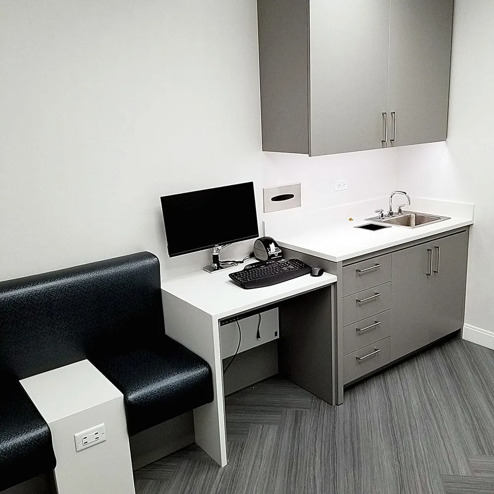 Grey plastic-laminate exam-room casework with an integrated sink and workstation