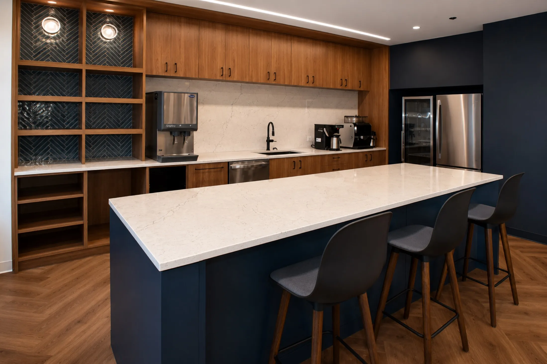 Corporate office pantry with a navy quartz-topped island, walnut cabinetry, and bar seating, fabricated by Pio